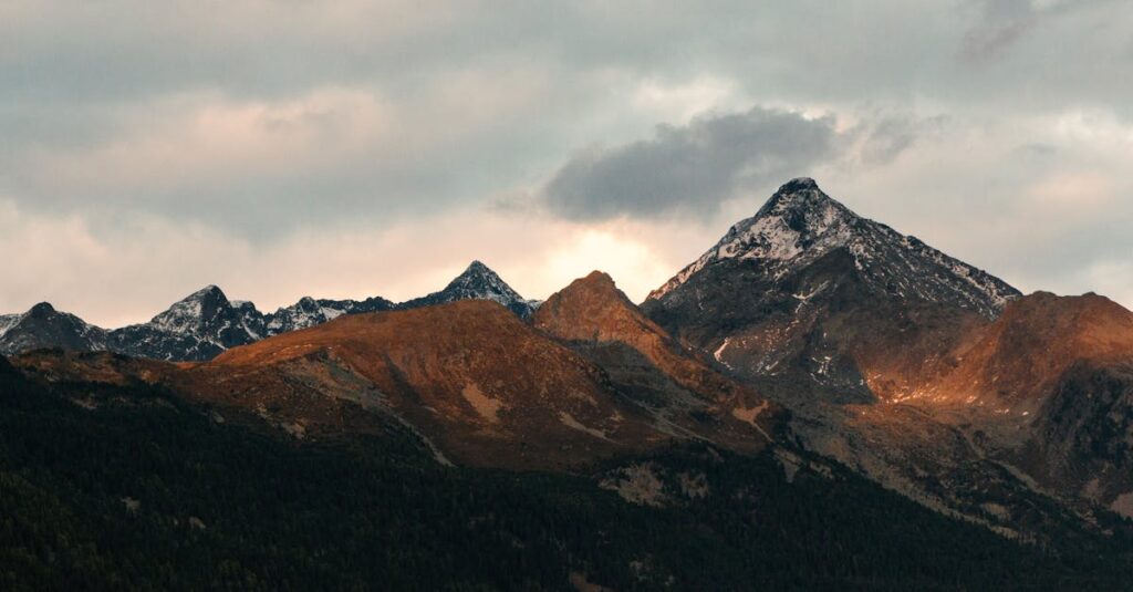 Breathtaking view of mountain peaks adorned with snow under a cloudy sky at dusk.